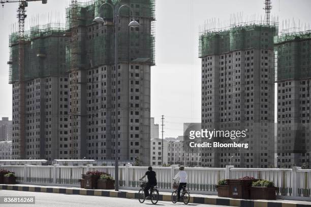 Commuters ride on bicycles past residential buildings under construction in Baotou, Inner Mongolia, China, on Friday, Aug. 11, 2017. China's economy...
