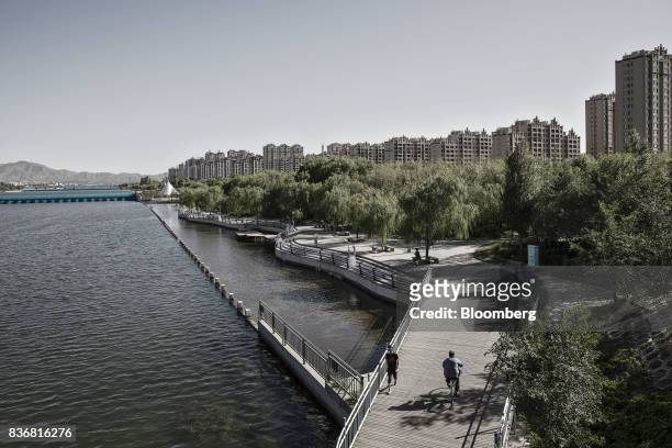 Man rides a bicycle over a bridge as new residential buildings stand in the distance in Baotou, Inner Mongolia, China, on Friday, Aug. 11, 2017....