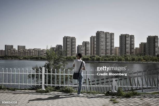 Man stands near the river banks across from new residential buildings in Baotou, Inner Mongolia, China, on Friday, Aug. 11, 2017. China's economy...