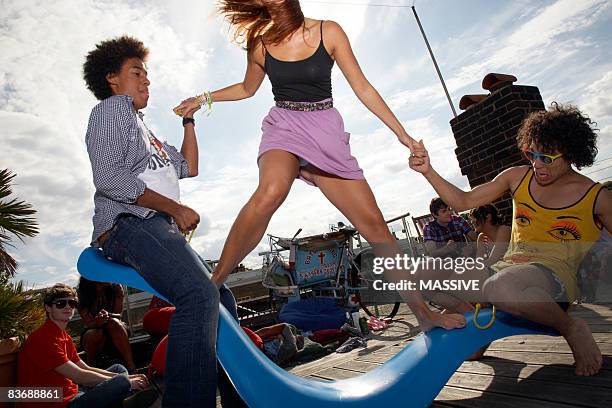 two guys help girl standing on seesaw - seesaw foto e immagini stock