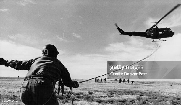 Helicopter hovers over Colorado army national guardsmen at Buckley air national guard base One paratrooper holds onto a rappelling rope as he directs...