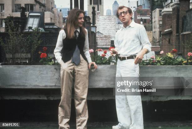 American actress Diane Keaton and film director, writer, and actor Woody Allen, each with a drink in their hands, talk together on a buildong rooftop...