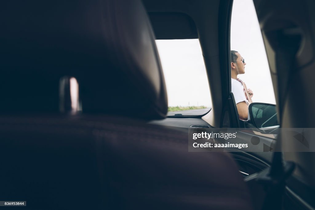 Young male playing guitar leaning on automobile