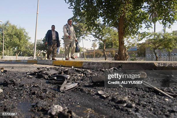 Iraqi men walk past the remains of damaged vehicles after a road side bomb detonated as a police convoy drove past in central Baghdad on November 15,...