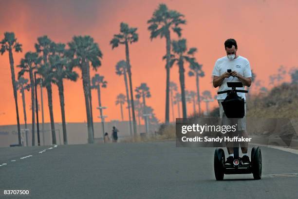 Man usues his cell phone while riding a Segway November 15, 2008 as the glow from a fire is seen in the distance in Yorba Linda, California. Strong...