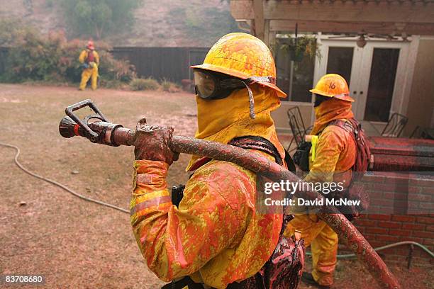 Firefighters are covered with red Phos-Check fire retardant dropped by a firefighting airtanker on the house they are protecting as wildfire closes...