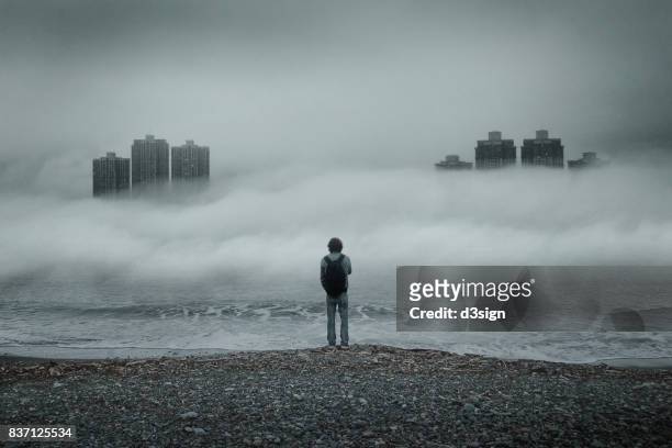Man standing alone looking out to sea against moody sky during foggy weather