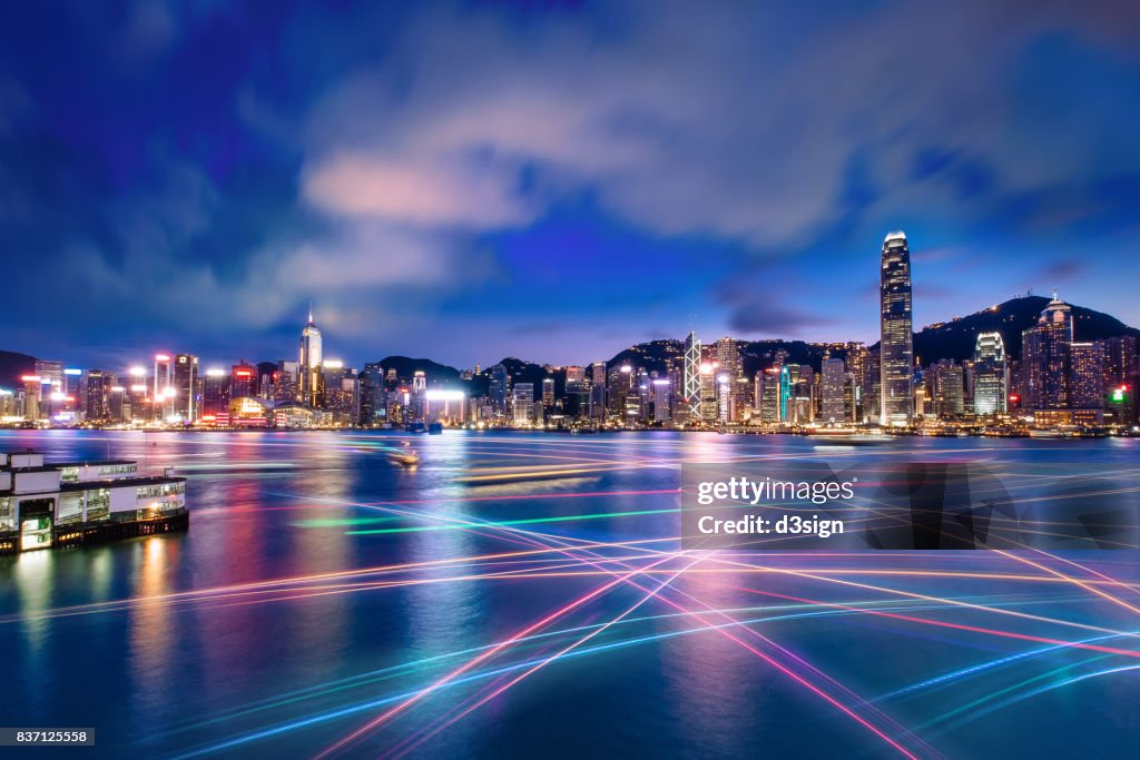 The world famous night scene of Hong Kong city skyline with busy water traffic navigate across Victoria Harbour