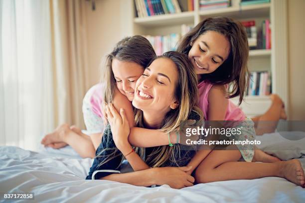 daughters are hugging their happy mom in the bed - good morning kiss images stock pictures, royalty-free photos & images