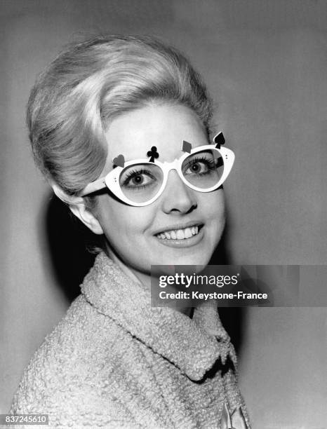 Une jeune femme, membre d'un club de bridge, porte des lunettes blanches décorées du coeur, carreau, trèfle et pique des cartes à jouer.