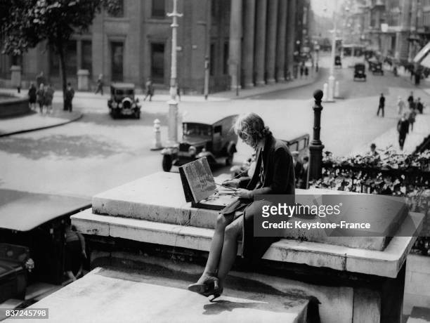 Une jeune femme peint Trafalgar Square assise sur les marches du musée la National Gallery le 22 août 1930 à Londres, Royaume-Uni.