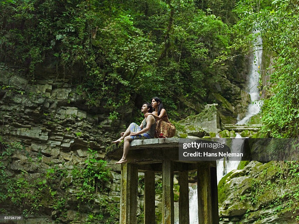 Couple sitting on ruin in jungle, looking up