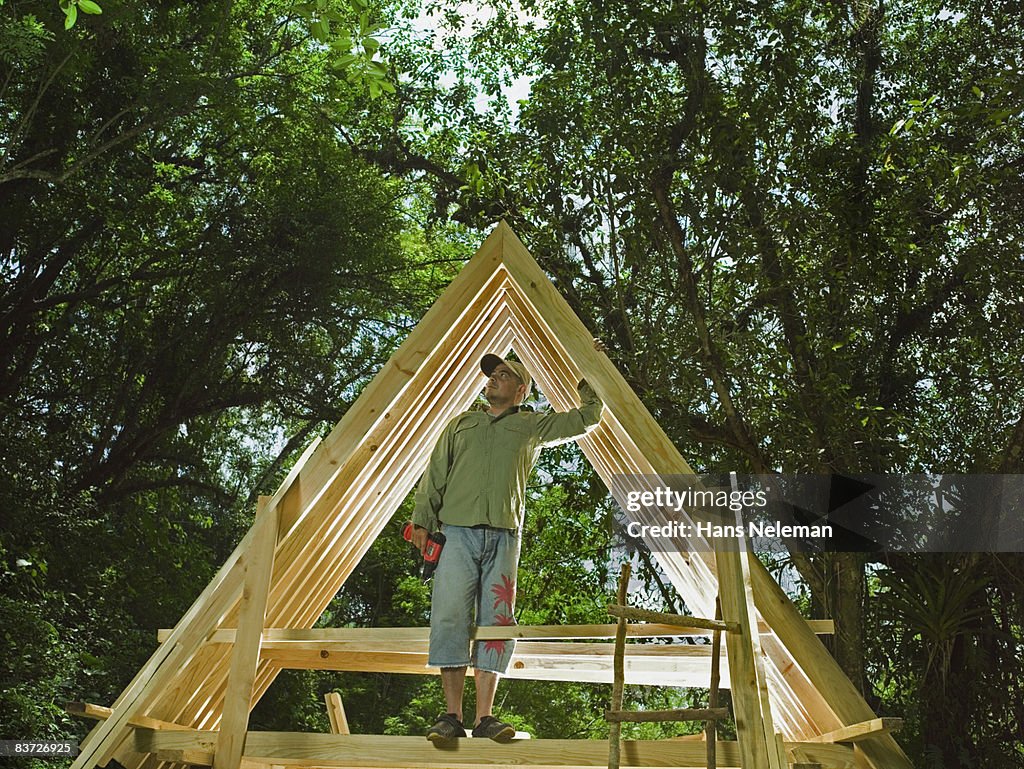 Man standing on frame of house in forest