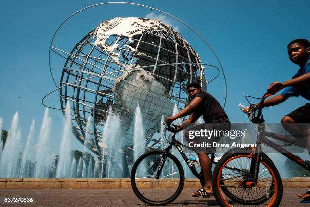 Two young boys ride their bikes past the fountains at the Unisphere steel structure at Flushing Meadows-Corona Park, August 22, 2017 in the Queens...