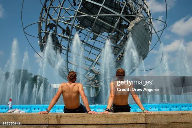 Two men take in the sun at the fountains by the Unisphere steel structure at Flushing Meadows-Corona Park, August 22, 2017 in the Queens borough of...