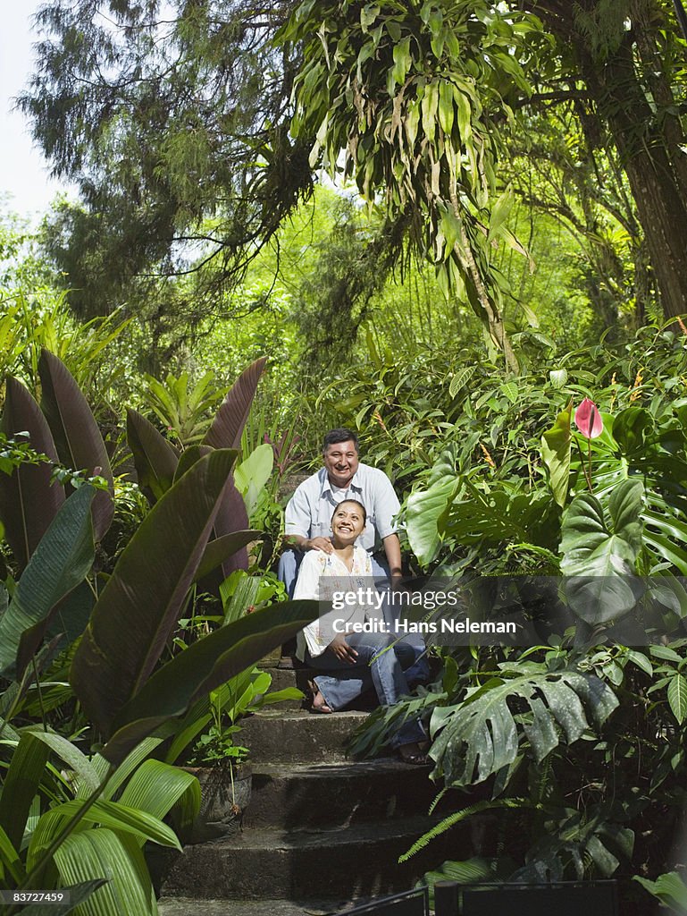 Couple sits on steps in lush garden