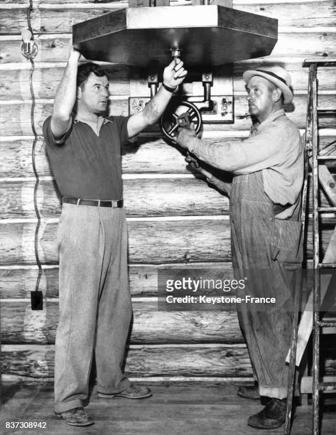 Le boxeur américain Jimmy Braddock aide un ouvrier à ajuster la plateforme de fixation d'un punching-bag au gymnase Karl Ogren le 8 avril 1937 à...