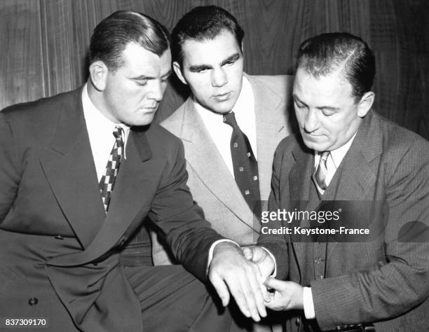 Dr George Edson, médecin de la commission de boxe, examine la main du boxeur américain Jimmy Braddock sous l'oeil attentif du boxeur Max Schmeling,...