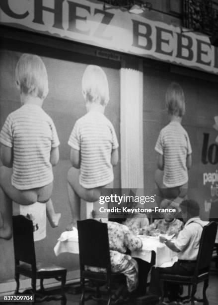 Des clientes attablées au restaurant 'Chez Bébert' près des Champs-Elysées tournent le dos à une immense affiche publicitaire 'Chez Bébé'...