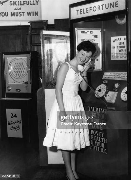 Une jeune femme écoute sa destinée prédite dans un combiné téléphonique par une cabine de téléfortune à la fête foraine de Worthing Pier à Worthing,...