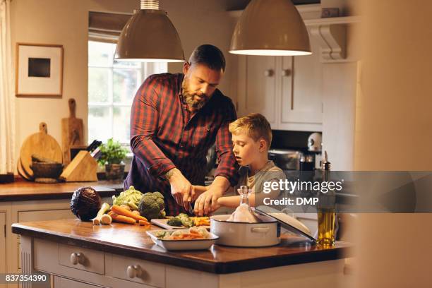 mann und kleiner junge schneiden frisches gemüse in der küche - bratengericht stock-fotos und bilder