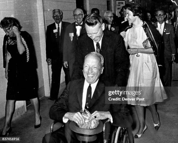 Postmaster General J. Edward Day Arrives At Stapleton In Wheel Chair His is being pushed by Charles Nicola, a Denver attorney. Day's wife, Mary...