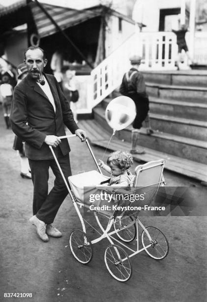 Un homme pousse son jeune enfant dans sa poussette à la fête foraine, circa 1920 en Allemagne.