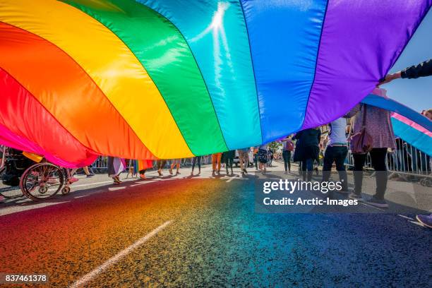 gay pride parade-people marching with a large flag, reykjavik, iceland - optocht stockfoto's en -beelden