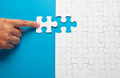 Hand holding piece of white puzzle on blue background.