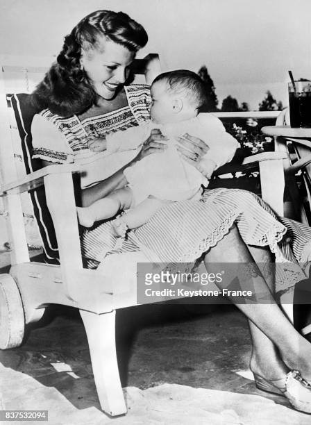 Actrice Rita Hayworth regarde admirative sa fille Rebecca Welles assise sur ses genoux, aux Etats-Unis en 1946.