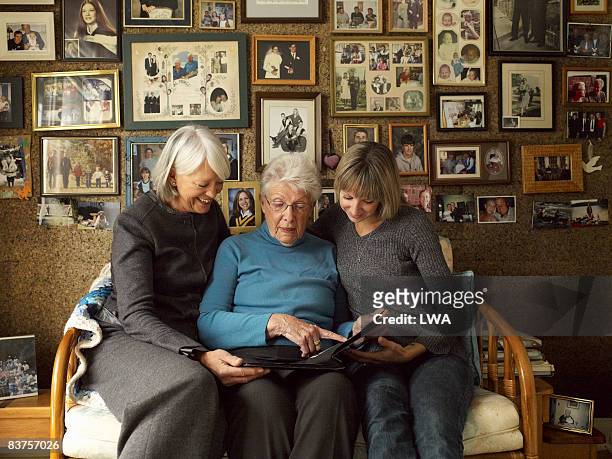 three generations of women looking at photo album - nostalgia fotografías e imágenes de stock