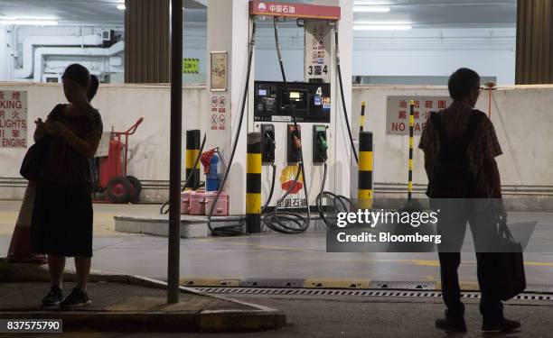 Pedestrians stand at a bus stop in front of a PetroChina Co. Gas station at night in Hong Kong, China, on Monday, Aug. 21, 2017. PetroChina is...