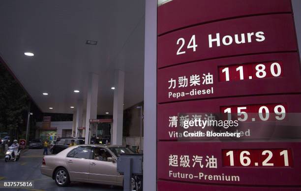 Vehicles stand while being refueled beyond a sign listing prices for various grades of fuel at a PetroChina Co. Gas station at night in Hong Kong,...
