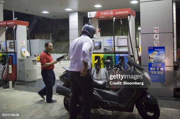 An employee collects payment from a customer after refueling a vehicle at a China Petroleum & Chemical Corp. Gas station at night in Hong Kong,...