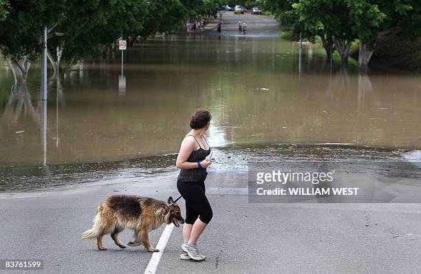 Woman walking her dog passes in front of a road flooded by the Bremer River in central Ipswich, some 50 kilometres west of Brisbane, on November 20,...