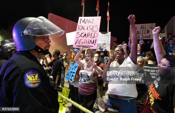 Phoenix police officer watches as a crowd of protesters outside the Phoenix Convention Center hold up signs and chant anti-Trump slogans during a...