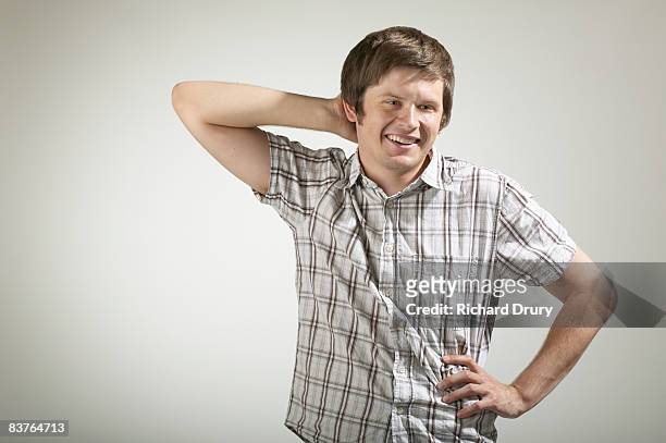 young man smiling with one hand behind head - embarrassment foto e immagini stock