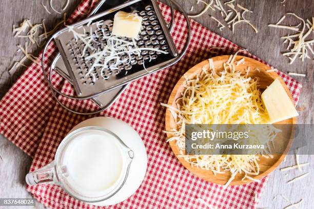 ingredients for pasta cheese sauce or pizza, freshly grated parmesan or cheddar hard cheese, raw milk in a pot, kitchen tools, grater, wooden plate and kitchen towel, rustic vintage style, top view - rallado fotografías e imágenes de stock