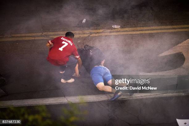 Demonstrator helps a man in a cloud of tear gas get up after collapsing as a line of police officers pepper spraying and tear gassing demonstrators...