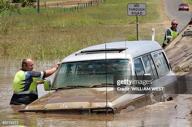 Two tow truck operators tow a four-wheel drive vehicle from the floods to dry ground some 80 kilometres west of Brisbane, on November 21 as flash...