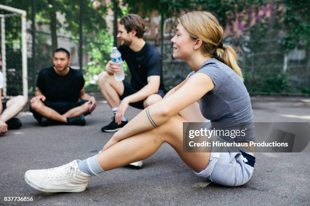 young athletic woman sitting down with friends to take a break from outdoor basketball match - germany womens training session stock pictures, royalty-free photos & images