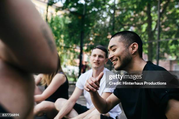 group of friends sitting down chatting before playing outdoor basketball together - city life authentic stockfoto's en -beelden