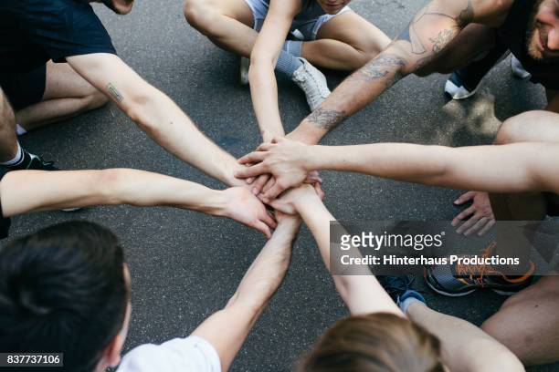 group of athletes bring hands together in unity before friendly outdoor basketball match - zusammenhalt stock-fotos und bilder