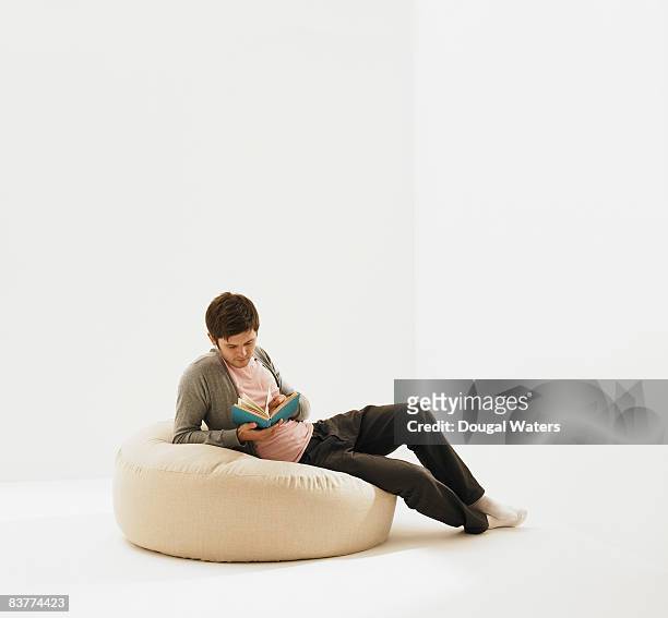 young man sitting on beanbag, reading. - beanbag photos et images de collection