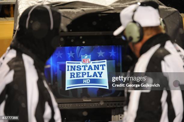 National Football League referee Ron Winter and side judge Tom Hill look at the instant replay monitor on the sideline as snow falls during a game...