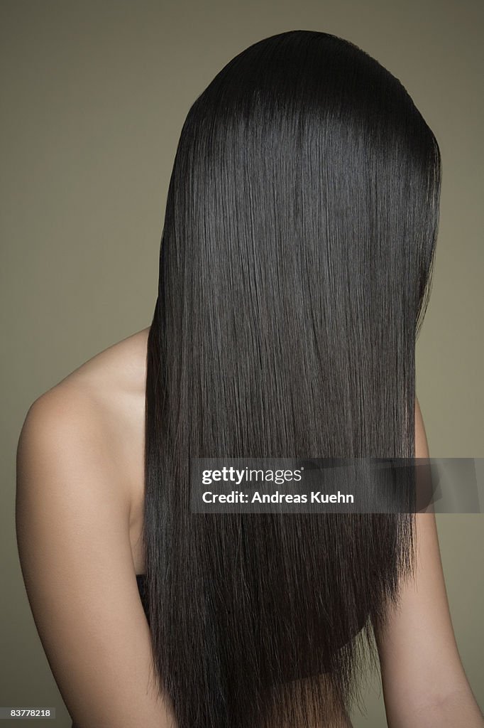 Woman with long, shiny hair covering face.