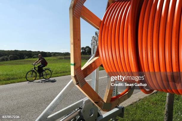 Man on a bicycle rides past a spool of tubing used for laying fiber optic cable underground during the installation of broadband infrastructure in...