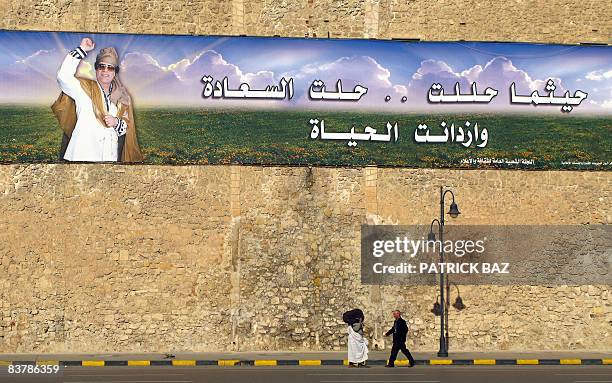 Libyans walk past a banner hailing Libya's leader Moamer Kadhafi on a wall in Tripoli's Green Square on November 21, 2008. AFP PHOTO/PATRICK BAZ