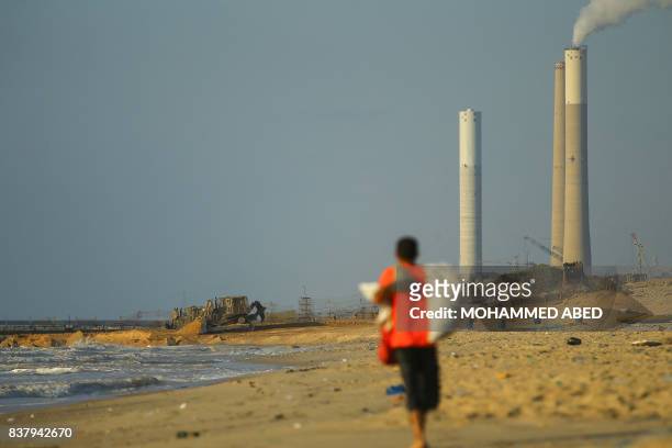 Picture taken on August 23, 2017 in Beit Lahia in the northern Gaza Strip shows a Palestinian walking along the beach as Israeli bulldozers dig...