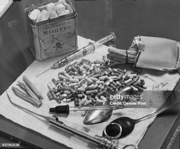 Confiscated narcotics and implements used by addicts are shown at Morals Bureau headquarters. Can contains a morphine compound. Capsules hold heroin....